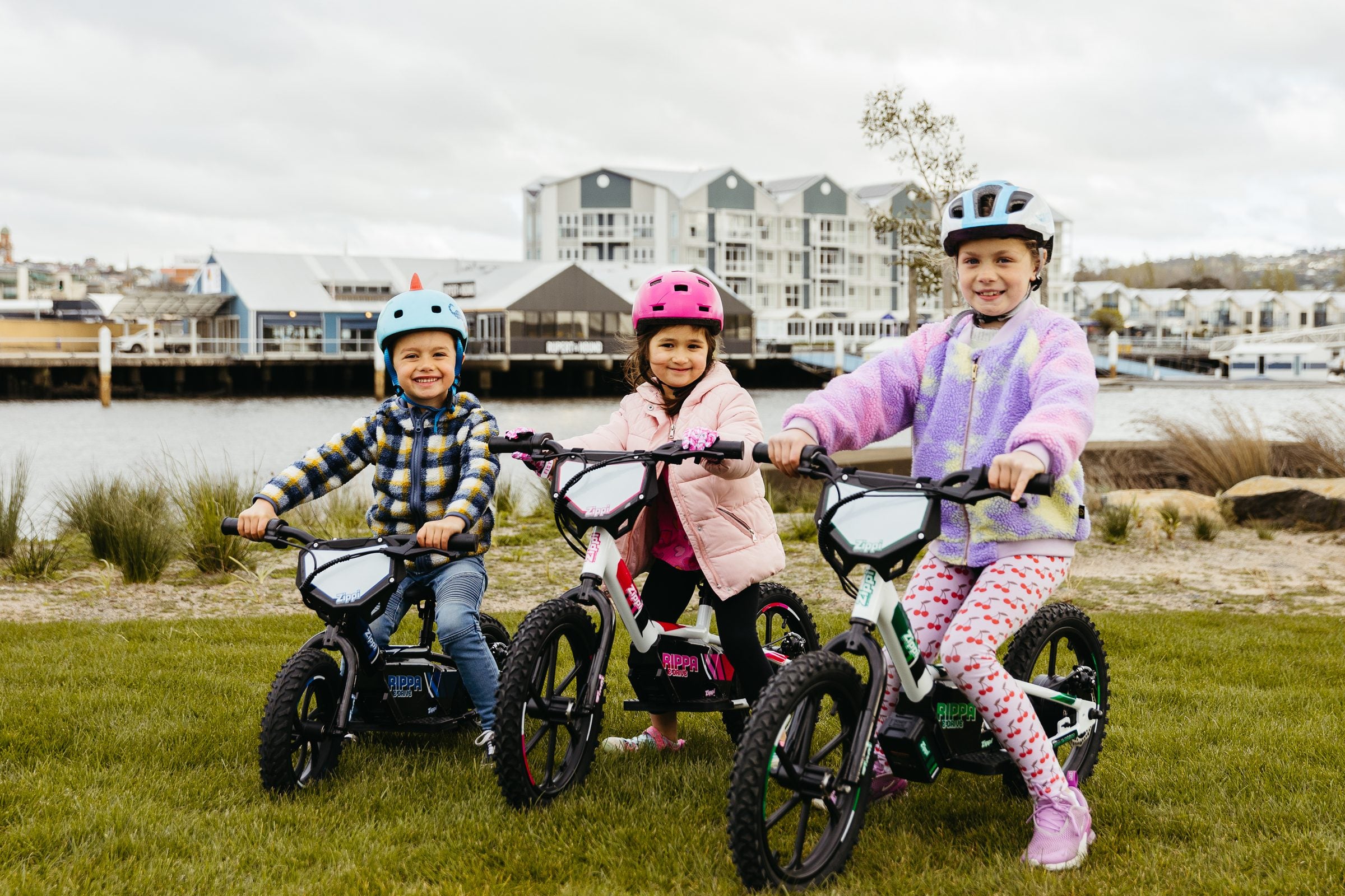 Three kids riding three sizes of Zippi bike on the riverside in Tasmania.