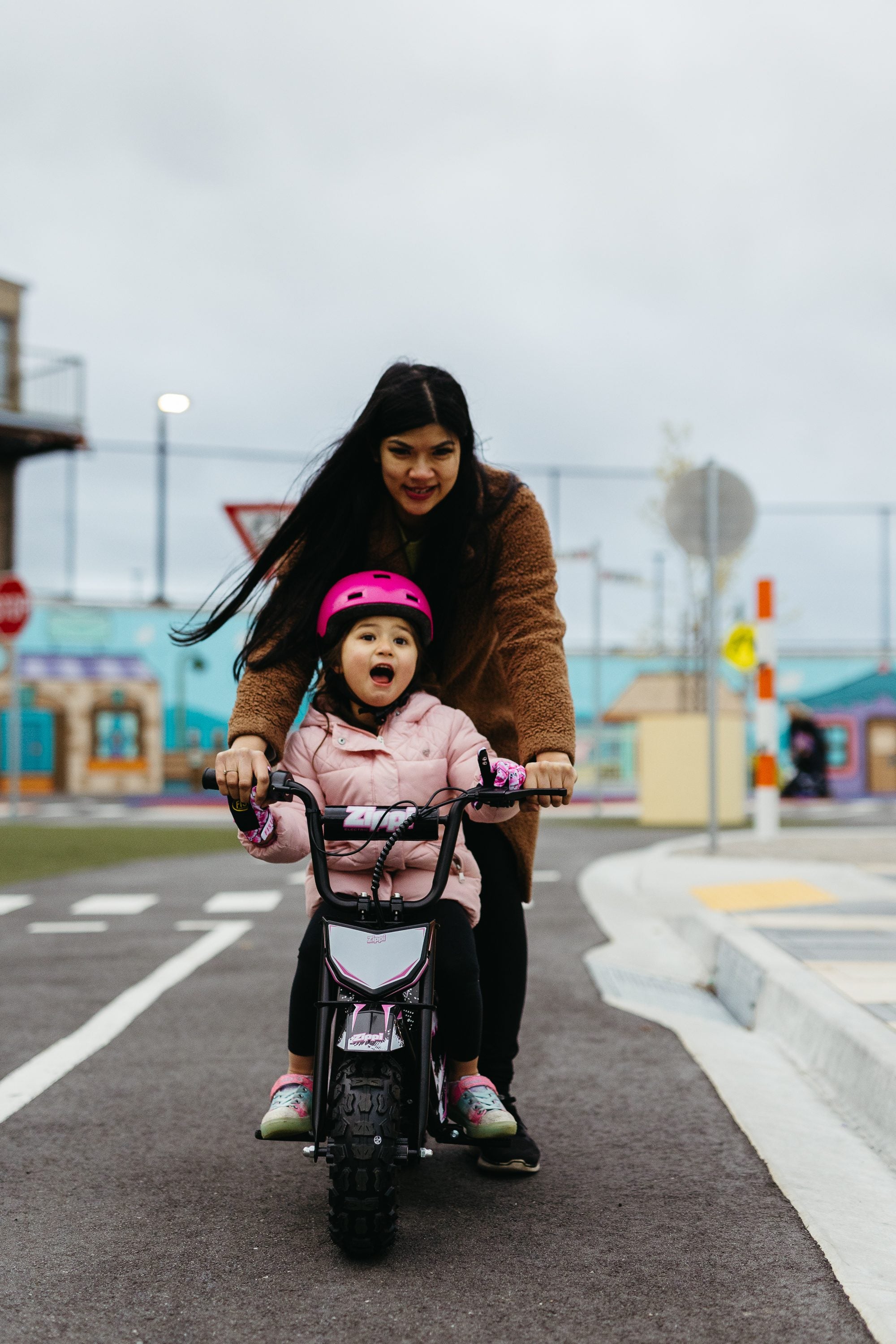 Mum standing behind her young daughter, both hands on the handlebars of a Zippi Rippa.